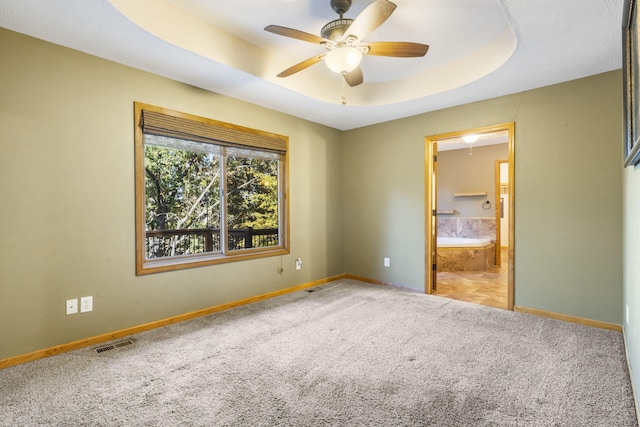 unfurnished bedroom featuring ceiling fan, a raised ceiling, light colored carpet, and ensuite bathroom