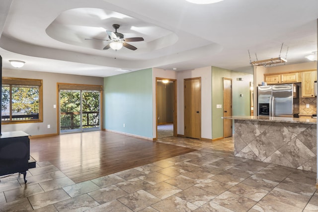 unfurnished living room featuring ceiling fan, a raised ceiling, and a wood stove