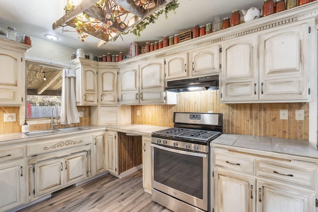 kitchen featuring cream cabinetry, light hardwood / wood-style floors, tile counters, sink, and stainless steel gas range