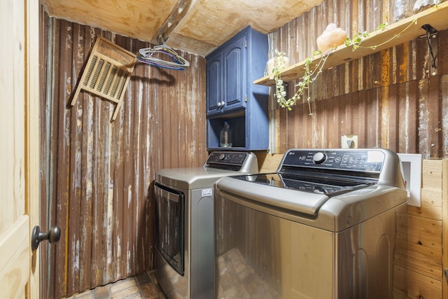 washroom with wood walls, washing machine and dryer, and cabinets