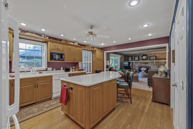 kitchen with black microwave, white dishwasher, a center island, a brick fireplace, and light hardwood / wood-style floors