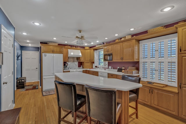 kitchen with a kitchen island, a breakfast bar area, ventilation hood, light wood-type flooring, and white appliances