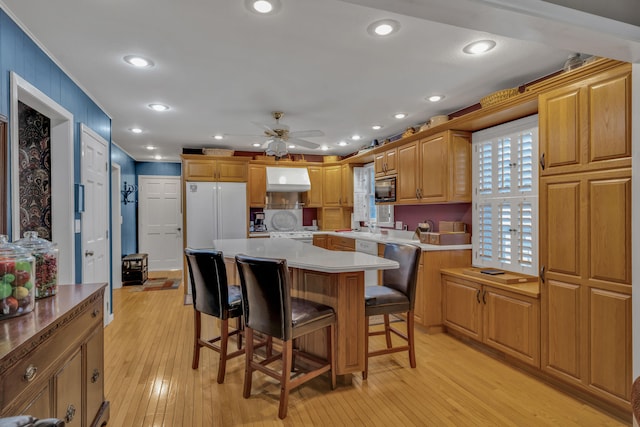 kitchen with a center island, a kitchen breakfast bar, white fridge, light hardwood / wood-style flooring, and black microwave