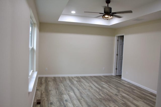 empty room featuring baseboards, wood finished floors, a ceiling fan, and a tray ceiling