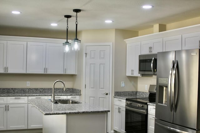 kitchen featuring a kitchen island with sink, a sink, stainless steel appliances, decorative light fixtures, and white cabinetry