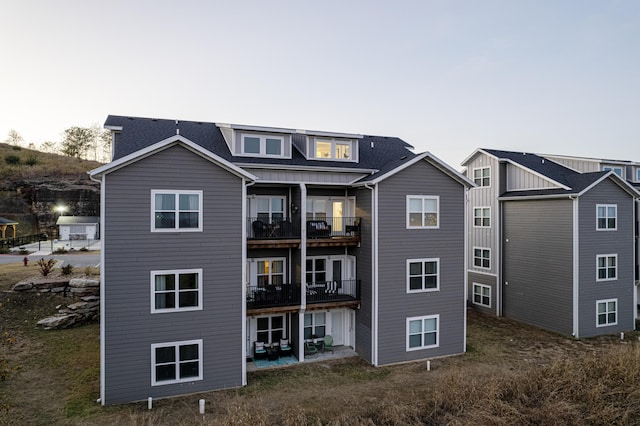 rear view of house featuring a shingled roof, a patio area, and a balcony