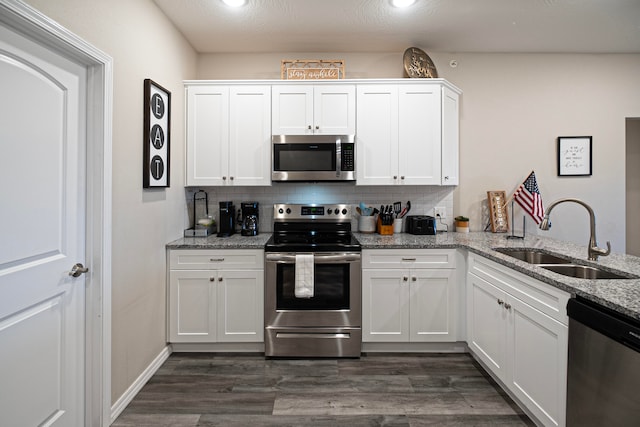 kitchen with appliances with stainless steel finishes, sink, dark hardwood / wood-style flooring, white cabinets, and light stone counters