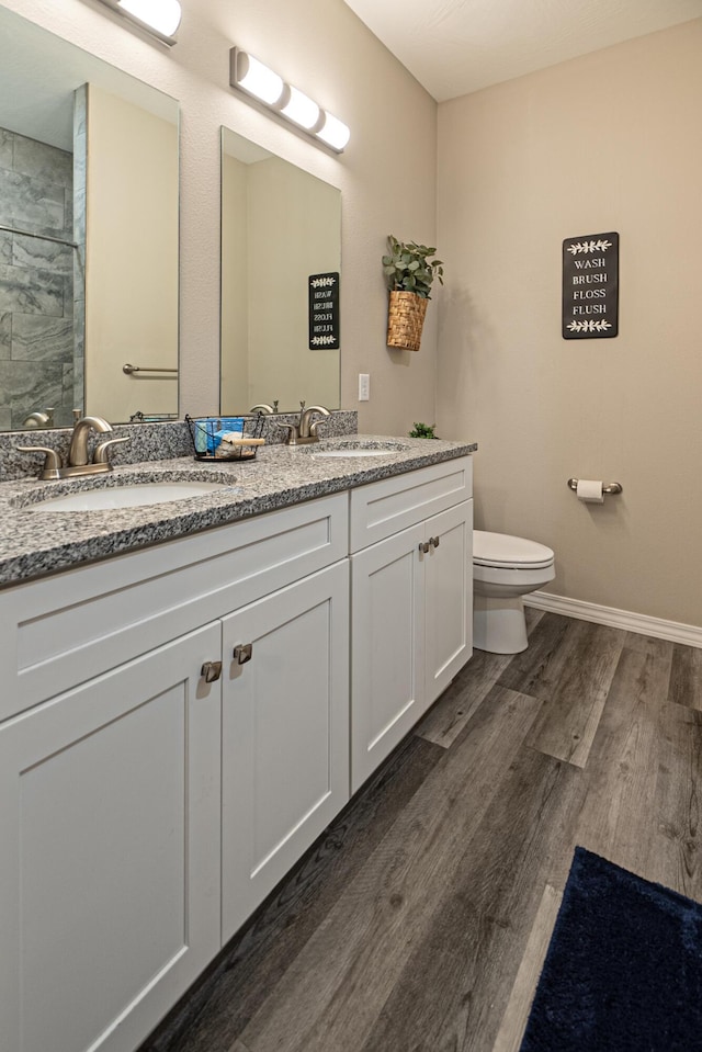 full bathroom with a sink, double vanity, toilet, and wood finished floors