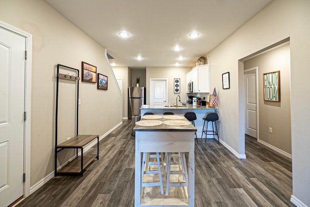 kitchen with appliances with stainless steel finishes, white cabinetry, a kitchen bar, dark wood-type flooring, and sink