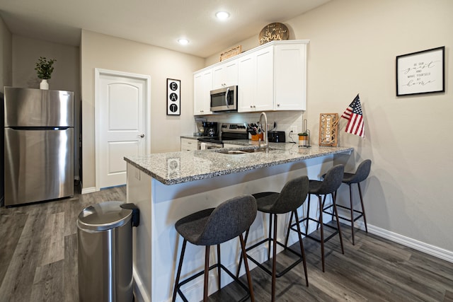 kitchen with sink, kitchen peninsula, white cabinetry, stainless steel appliances, and light stone counters