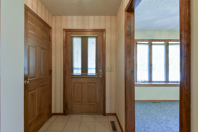 doorway with a textured ceiling, a healthy amount of sunlight, and light tile patterned floors