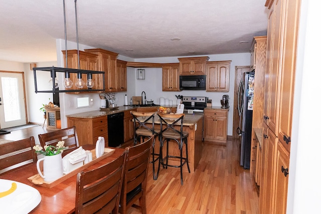 kitchen featuring a kitchen island, a breakfast bar area, light hardwood / wood-style flooring, hanging light fixtures, and black appliances