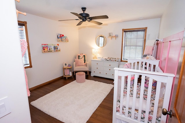 bedroom featuring a nursery area, dark hardwood / wood-style floors, and ceiling fan