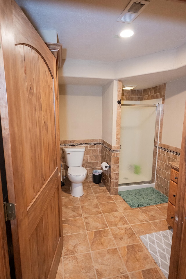 bathroom with toilet, a shower with shower door, and tile walls