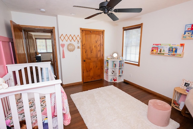 bedroom featuring dark hardwood / wood-style floors, a crib, and ceiling fan