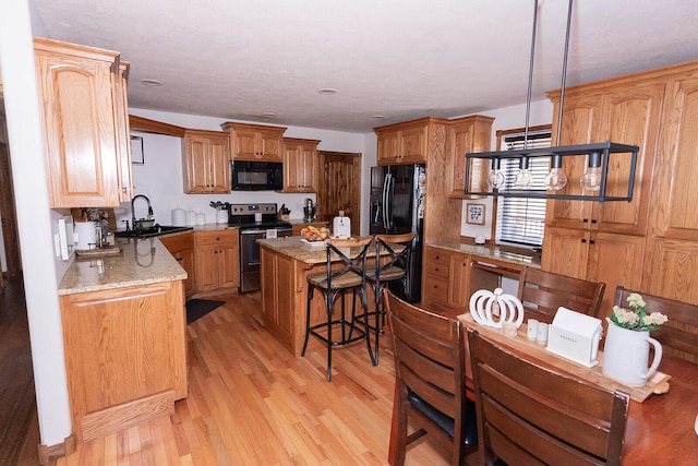 kitchen featuring black appliances, sink, a kitchen island, hanging light fixtures, and light hardwood / wood-style flooring