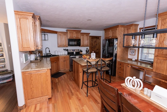 kitchen featuring light stone counters, light hardwood / wood-style flooring, black appliances, sink, and a center island