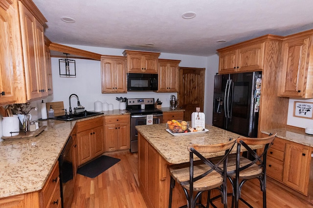 kitchen featuring black appliances, sink, a kitchen bar, light hardwood / wood-style floors, and light stone counters