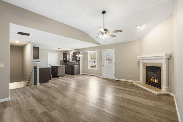 unfurnished living room with a tiled fireplace, dark hardwood / wood-style floors, vaulted ceiling, a textured ceiling, and ceiling fan