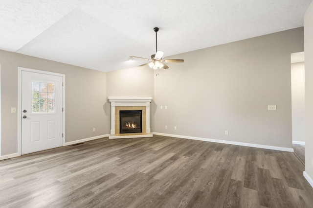 unfurnished living room featuring hardwood / wood-style floors, a textured ceiling, a tile fireplace, and ceiling fan