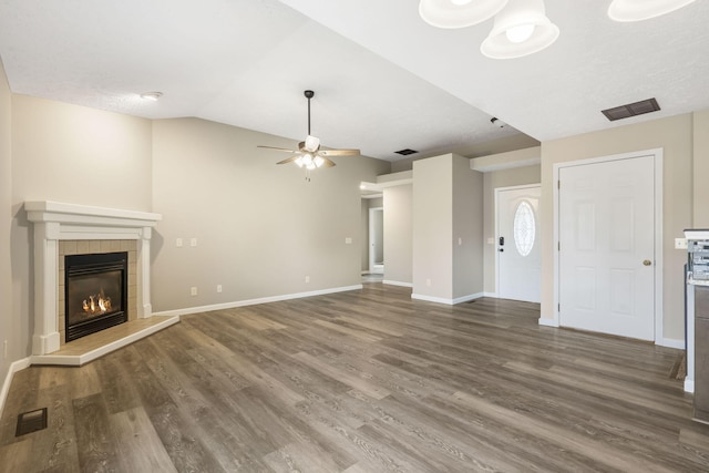 unfurnished living room featuring lofted ceiling, ceiling fan, a tile fireplace, and dark hardwood / wood-style flooring