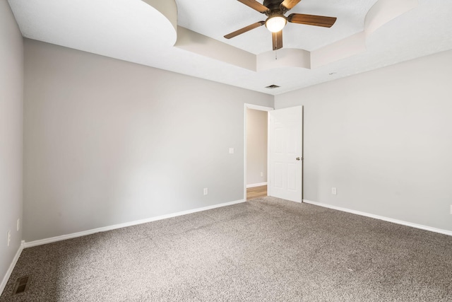 carpeted spare room with ceiling fan and a raised ceiling