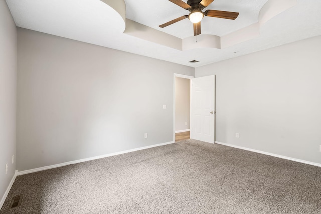 carpeted spare room with baseboards, visible vents, a raised ceiling, and ceiling fan