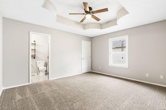 unfurnished bedroom with ceiling fan, a raised ceiling, carpet flooring, ensuite bathroom, and a closet