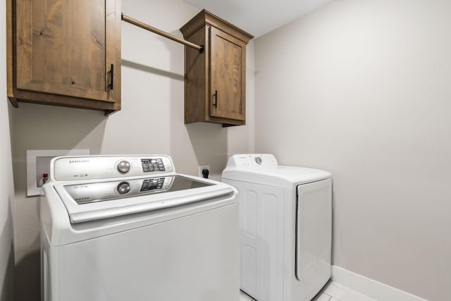 laundry area featuring washer and clothes dryer, light tile patterned floors, and cabinets