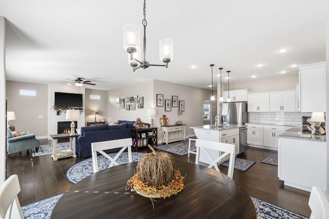 dining area with sink, ceiling fan with notable chandelier, a fireplace, and dark hardwood / wood-style flooring