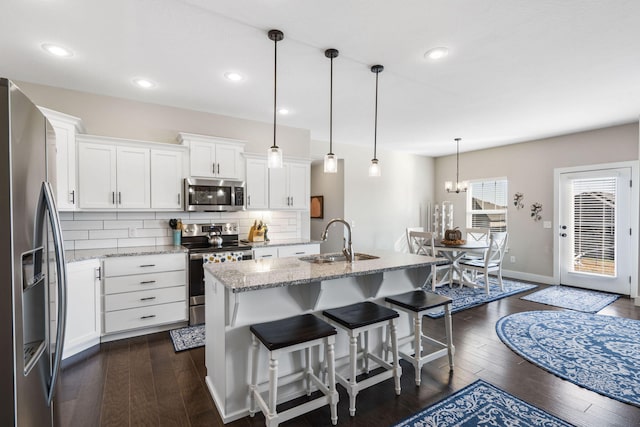 kitchen with white cabinets, dark hardwood / wood-style flooring, stainless steel appliances, decorative light fixtures, and light stone counters