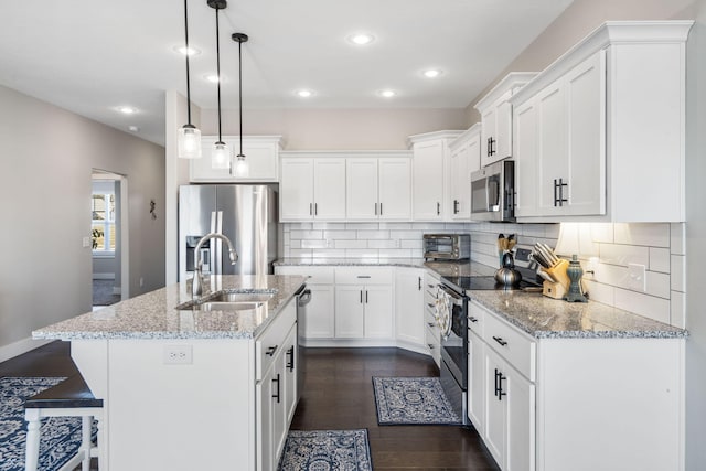 kitchen with appliances with stainless steel finishes, dark hardwood / wood-style flooring, hanging light fixtures, white cabinetry, and a center island with sink