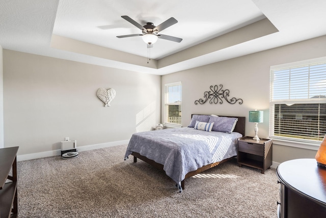 carpeted bedroom featuring multiple windows, a raised ceiling, and ceiling fan