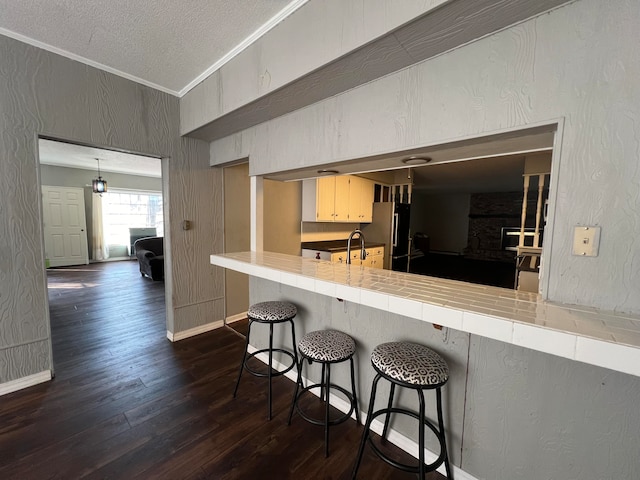 kitchen featuring tile countertops, a breakfast bar area, kitchen peninsula, refrigerator, and dark hardwood / wood-style flooring