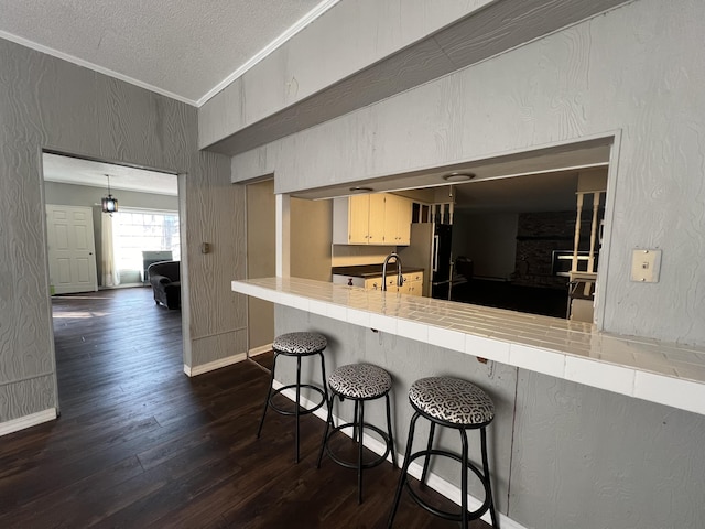 kitchen with freestanding refrigerator, a kitchen breakfast bar, a textured ceiling, crown molding, and dark wood-style flooring