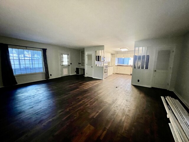 unfurnished living room with baseboards and dark wood-type flooring