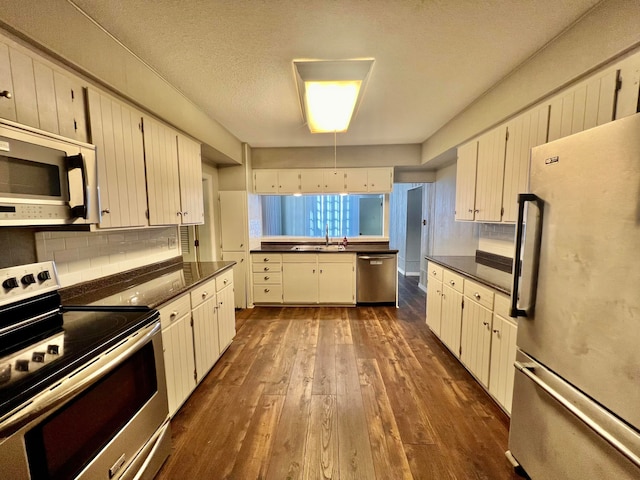 kitchen with dark hardwood / wood-style floors, stainless steel appliances, white cabinets, a textured ceiling, and tasteful backsplash