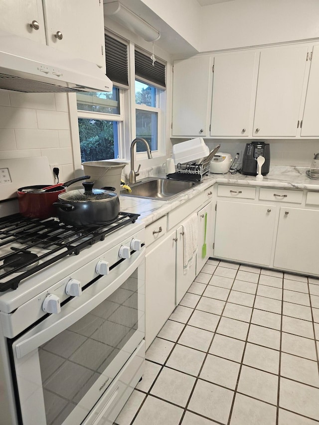 kitchen featuring light tile patterned flooring, white cabinets, gas range gas stove, and sink