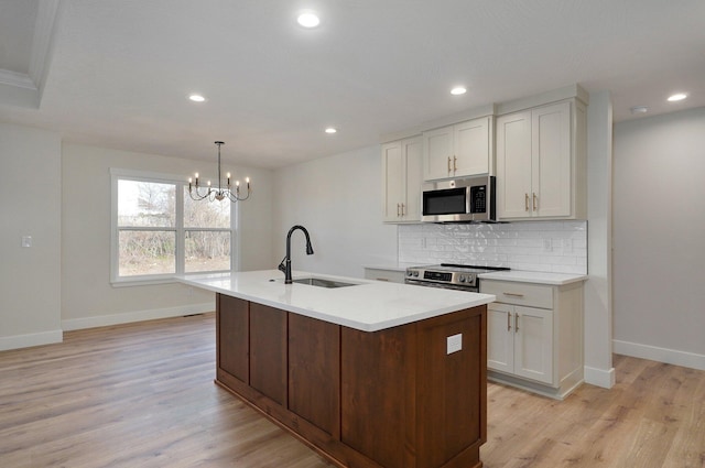 kitchen featuring a kitchen island with sink, sink, stainless steel appliances, and light wood-type flooring