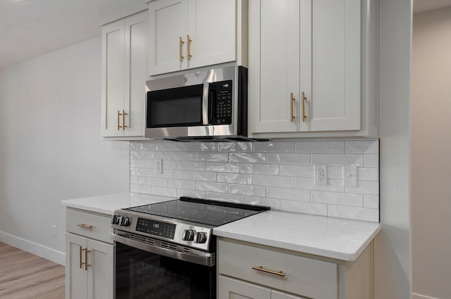 kitchen with stainless steel appliances, tasteful backsplash, light stone counters, light hardwood / wood-style flooring, and white cabinets