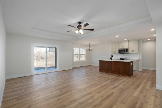 kitchen featuring white cabinets, light wood-type flooring, ceiling fan with notable chandelier, and an island with sink