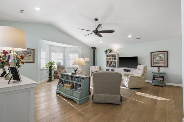 living room with lofted ceiling, light hardwood / wood-style flooring, a wood stove, and ceiling fan