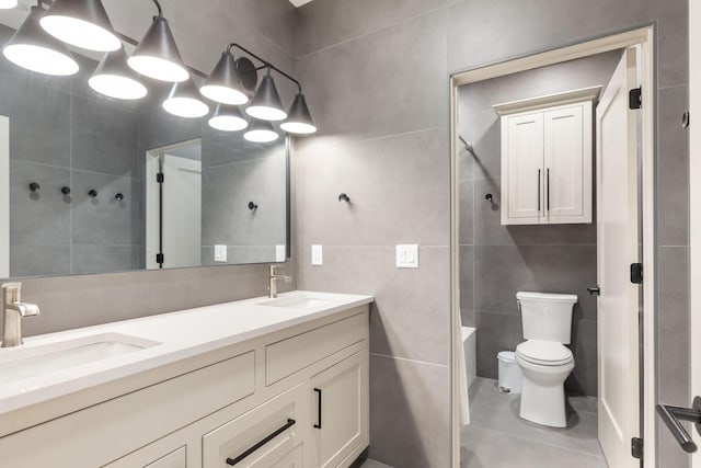 full bathroom featuring toilet, tile walls, double vanity, and a sink
