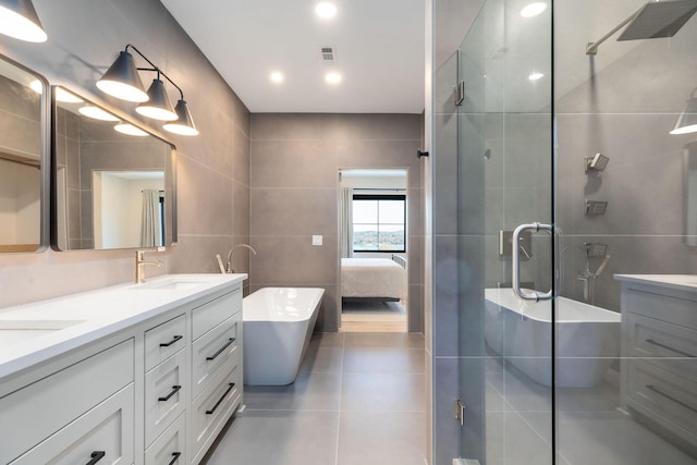 full bath with a sink, tile walls, tile patterned flooring, a shower stall, and double vanity