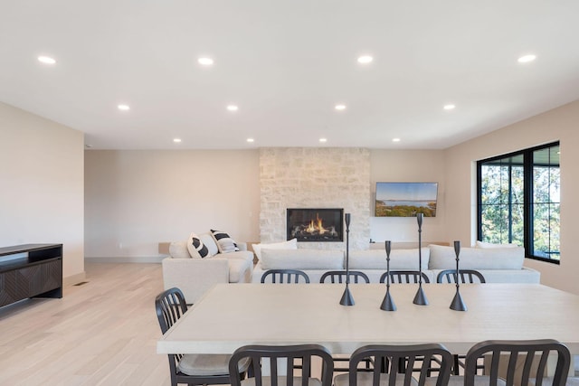 dining space featuring light wood finished floors, baseboards, a stone fireplace, and recessed lighting
