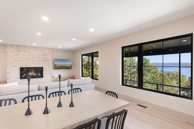 dining room featuring a water view, wood finished floors, visible vents, a stone fireplace, and recessed lighting