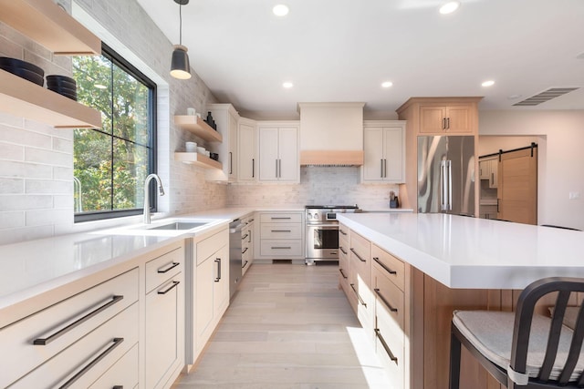 kitchen featuring a sink, open shelves, premium appliances, a barn door, and premium range hood