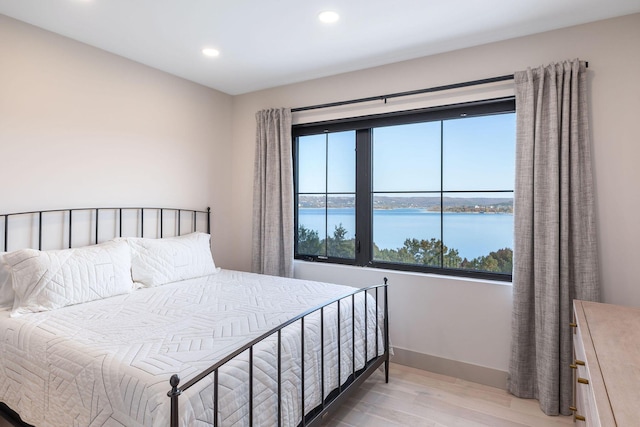 bedroom with baseboards, light wood finished floors, recessed lighting, and a water view