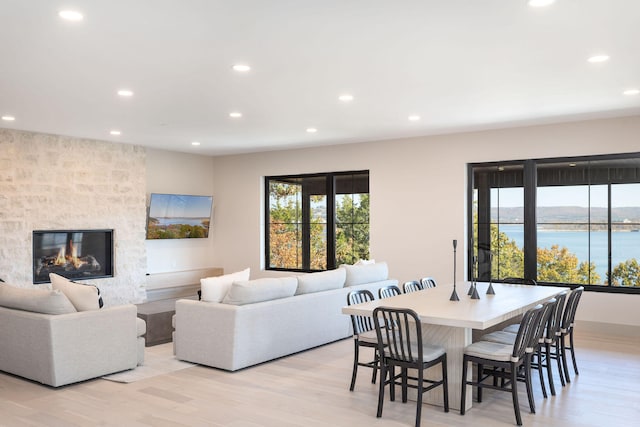 dining room with a stone fireplace, light hardwood / wood-style flooring, and a water view