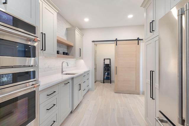 kitchen with white cabinetry, a barn door, light hardwood / wood-style flooring, sink, and stainless steel appliances